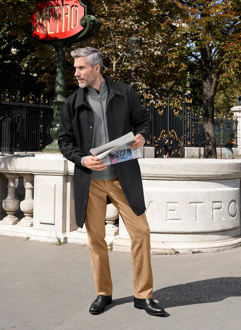 Mann in Wollmantel, steht vor einem Metro-Schild in Paris.