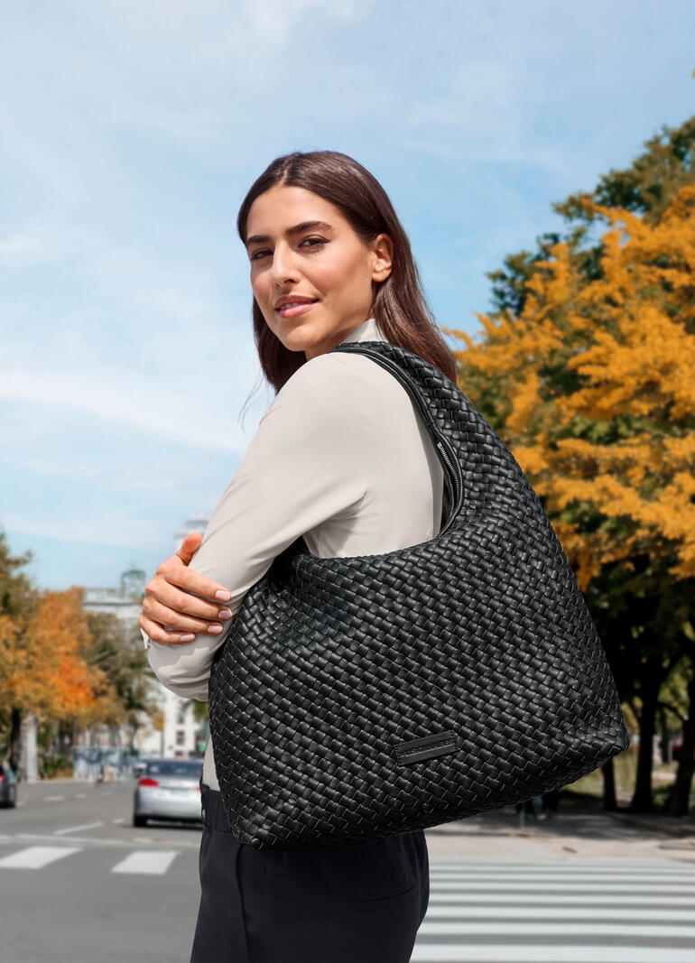 Frau trägt schwarze Hobo-Flechttasche auf einer belebten Straße im Herbst.