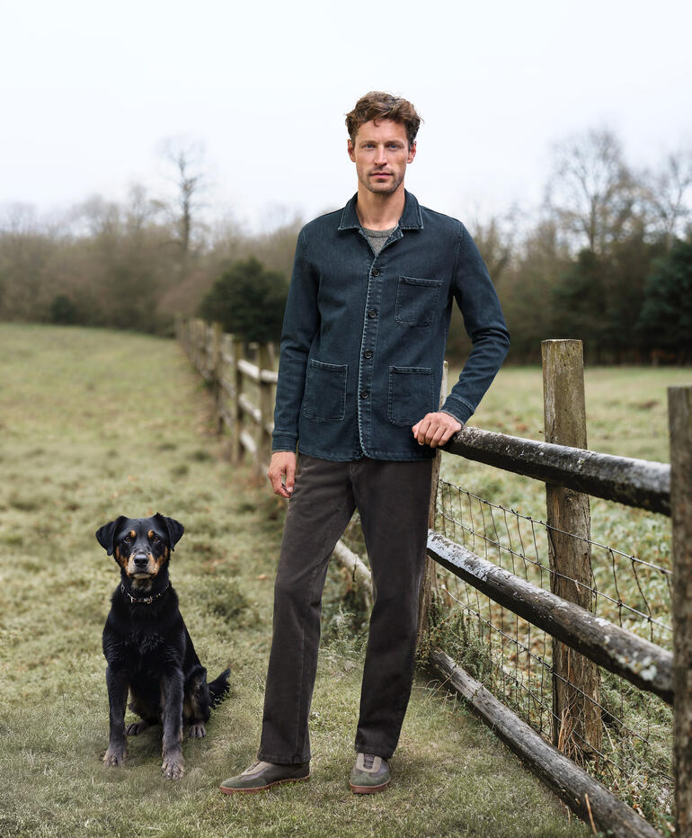 Mann trägt Kaschmir Denim Shacket und steht neben einem Hund auf einer Wiese.