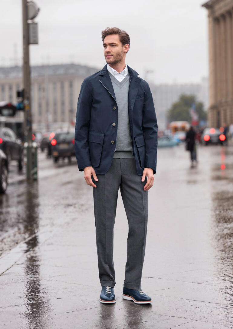 Dunkelblaue Allwetter-Jacke für Herren, stehend auf einer regnerischen Straße.