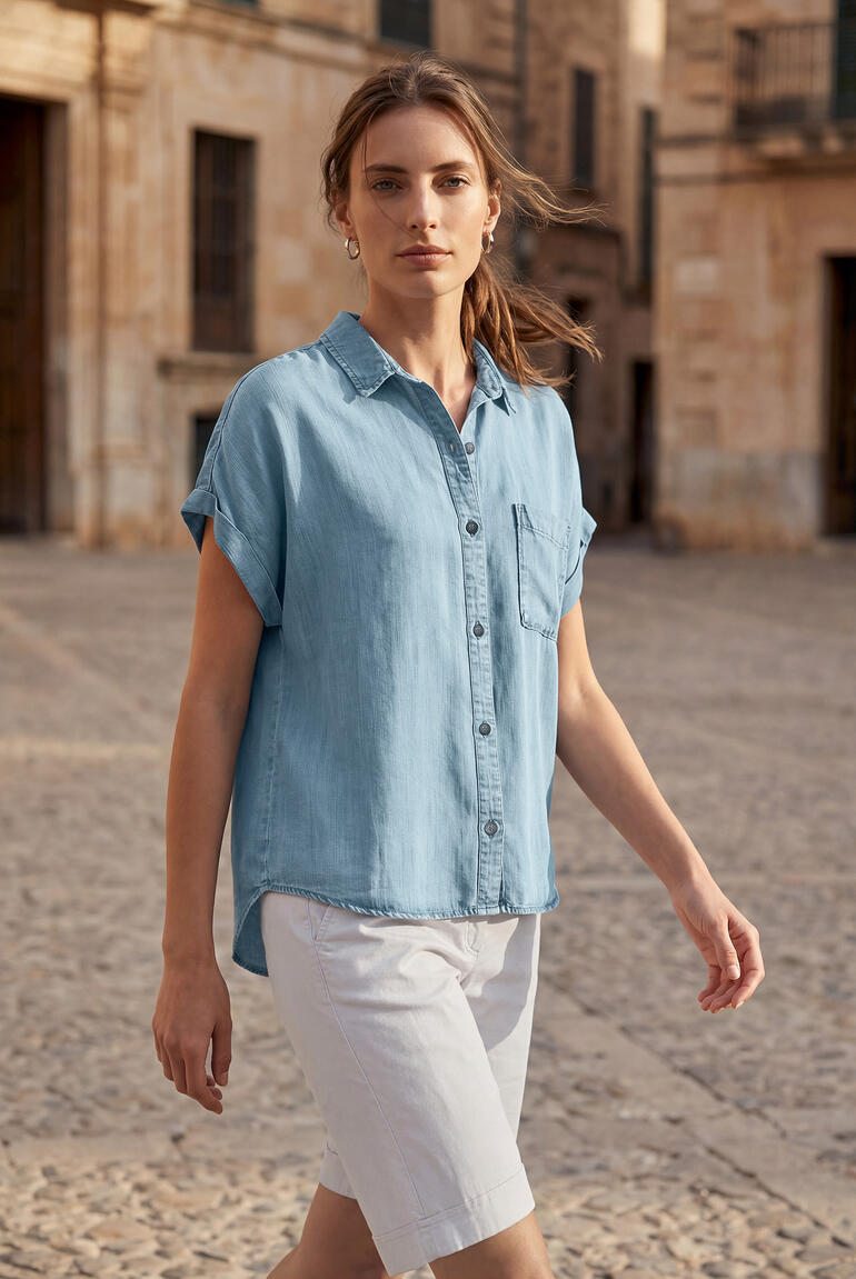 Frau in einer blauen Kurzarm-Soft-Jeansbluse geht selbstbewusst auf einer Straße.
