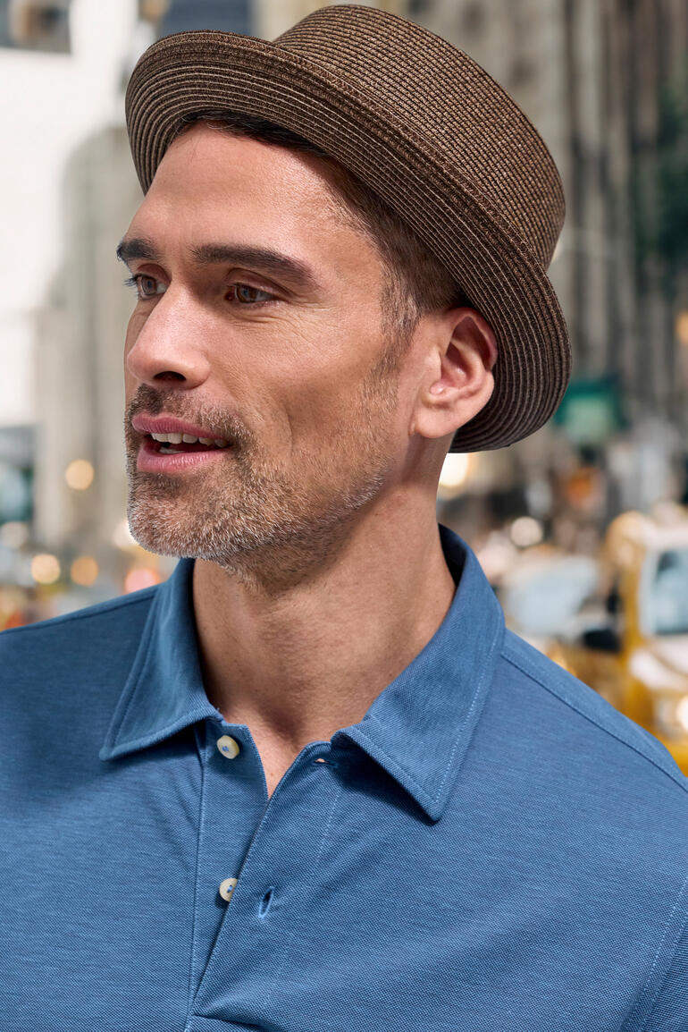 Mann mit braunem Pork Pie Hut und blauem Poloshirt.