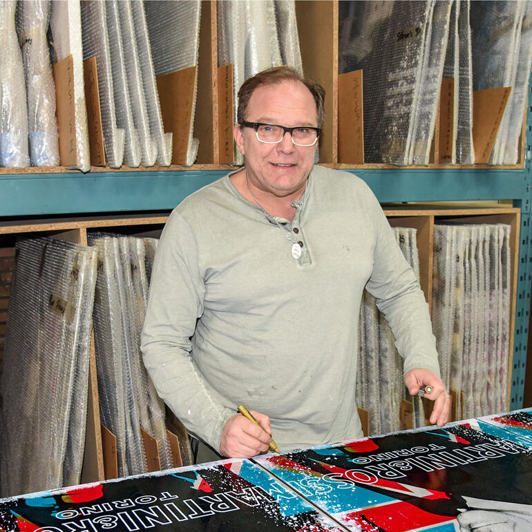 Devin Miles lächelt, während er an einem Tisch mit bunten Druckpostern arbeitet.