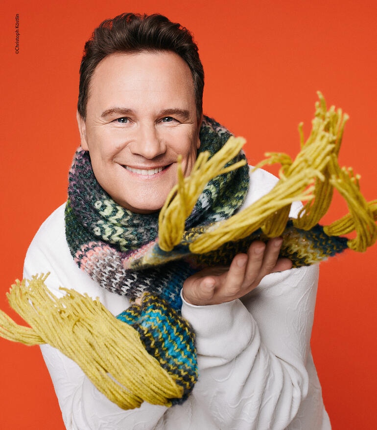 Charity Paket mit einem bunten Schal, präsentiert von einem lächelnden Mann.