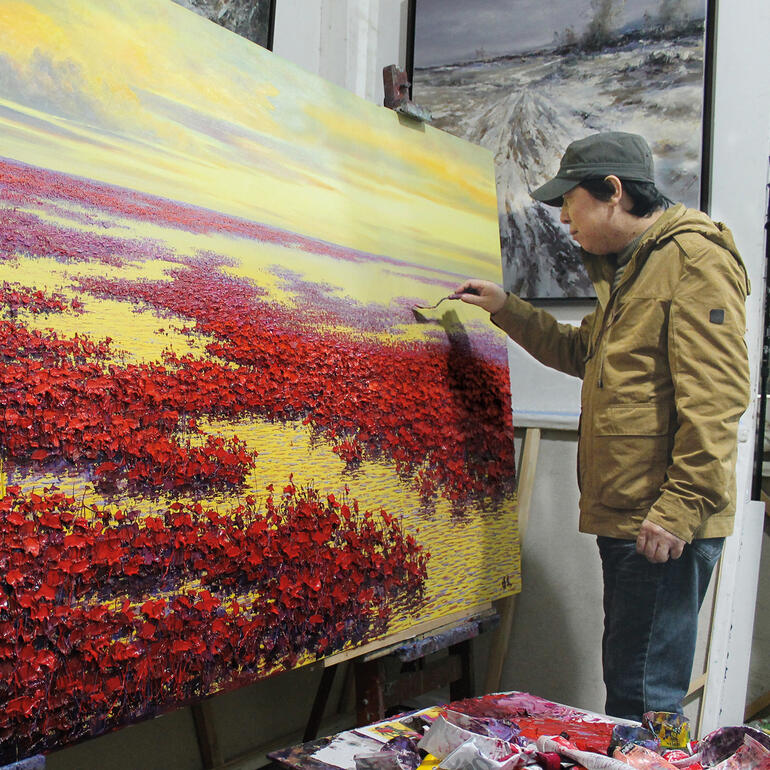 Pei Lian Zhi in seinem Atelier. Künstler Pei Lian Zhi malt an einem großen rot-blühenden Gemälde.