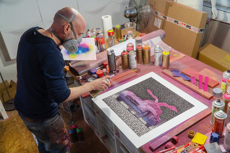 SAXA Künstler arbeitet an einem Bild, umgeben von verschiedenen Kunstmaterialien.