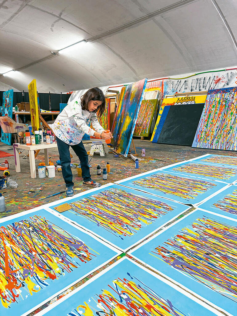 Mikail Akar Künstlerin bei der Arbeit an mehreren farbigen Kunstwerken in einem Atelier.