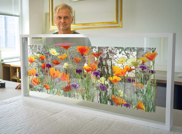 Künstlerin steht hinter einem Kunstwerk mit Blumenmotiven.