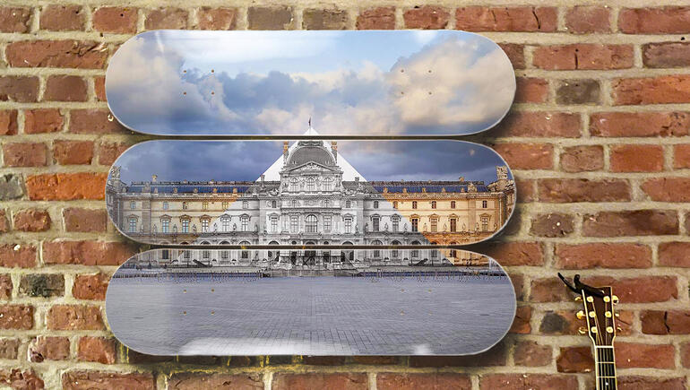 Drei Skateboard-Decks mit dem Louvre, an einer Backsteinmauer aufgestellt, neben einer Gitarre.