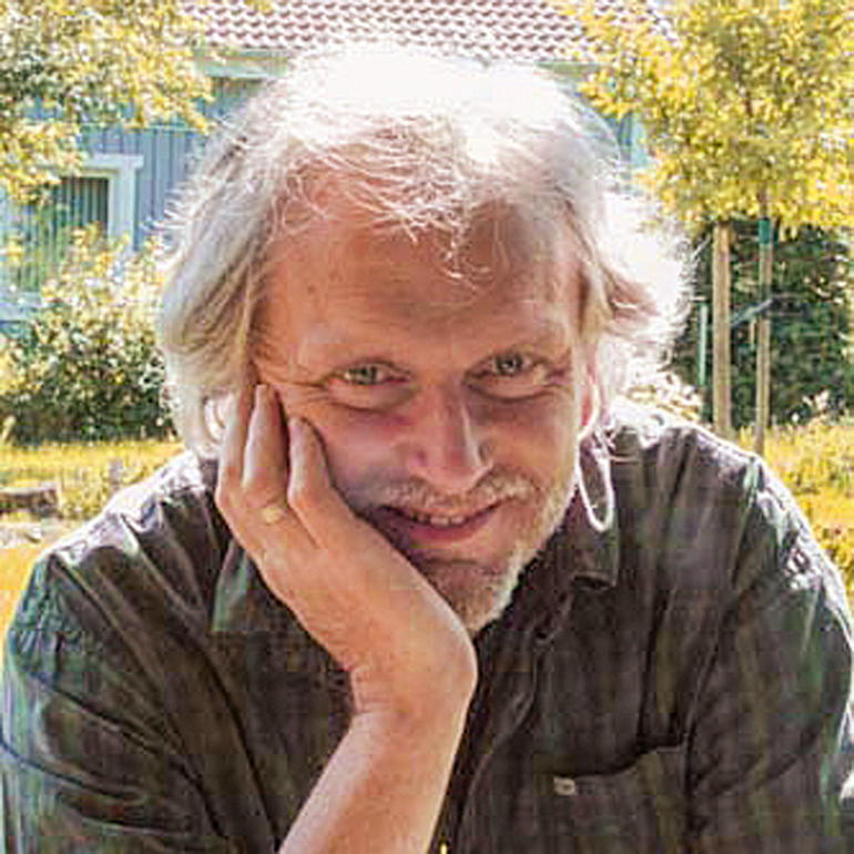 Mann mit grauen Haaren lächelt und stützt sein Kinn mit der Hand.