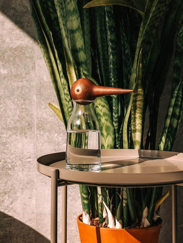 Glas wasser mit hölzernem Wasserspender in Form eines Vogels auf einem Tisch.