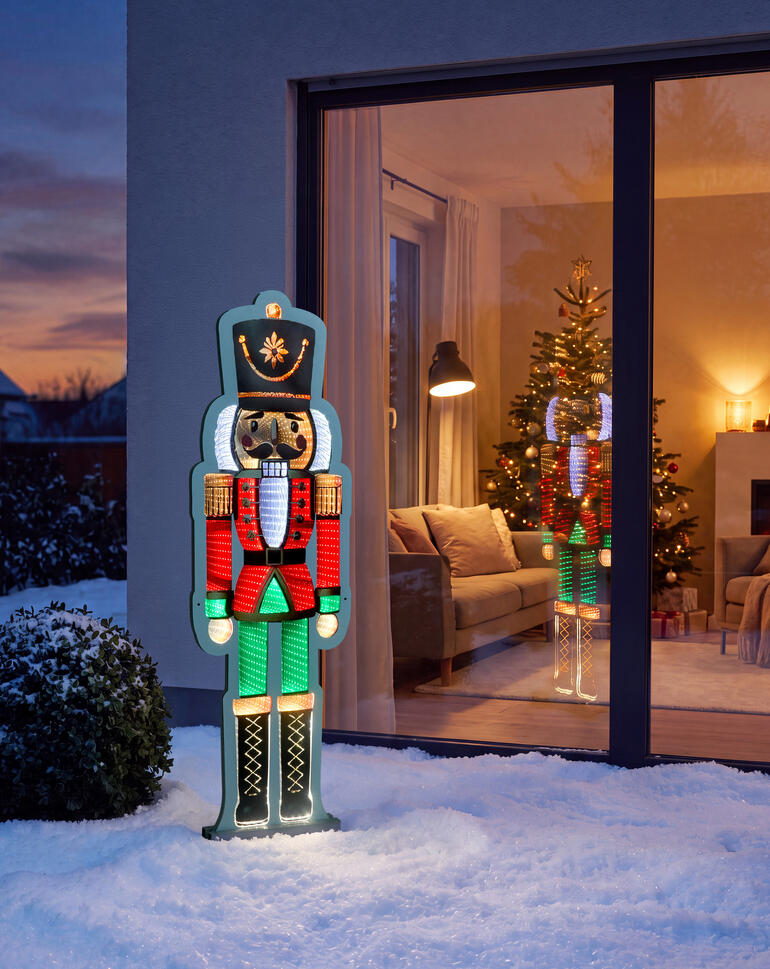 Nussknacker im Freien vor einem festlich geschmückten Fenster mit Weihnachtsbaum.