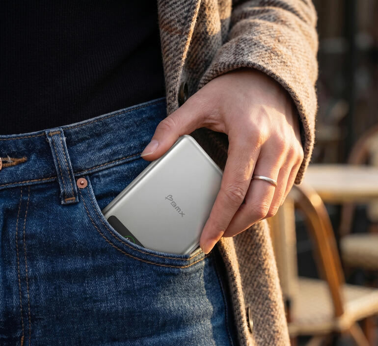 Eine Hand steckt eine silberne Powerbank in die Hosentasche.
