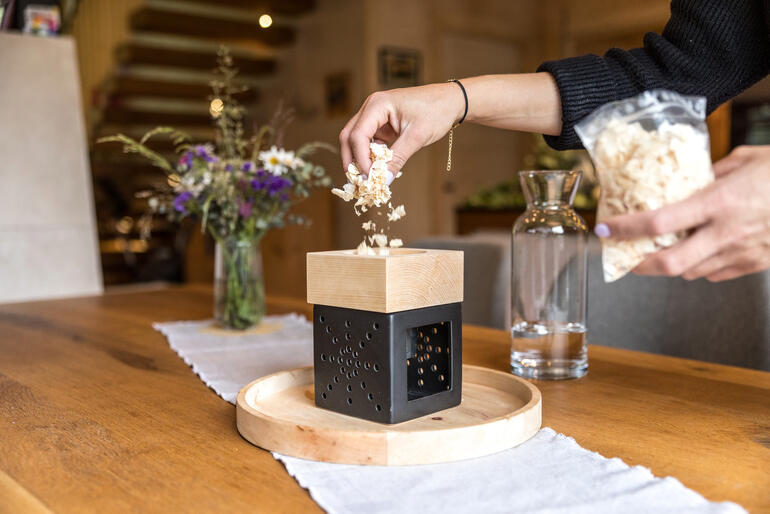 Person fügt Holzspäne in ein Zirbenholz-Kraftwerk auf einem Tisch ein.