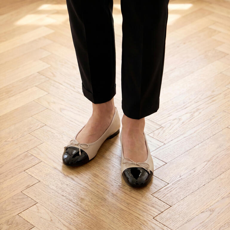 Beige Ballerinas mit schwarzem Zehenbereich auf einem hölzernen Boden
