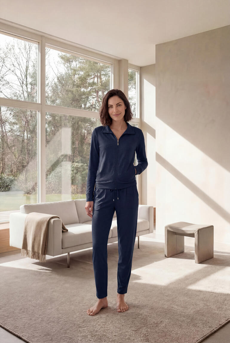 Frau steht in einem grauen Modal-Hausanzug vor einem großen Fenster.