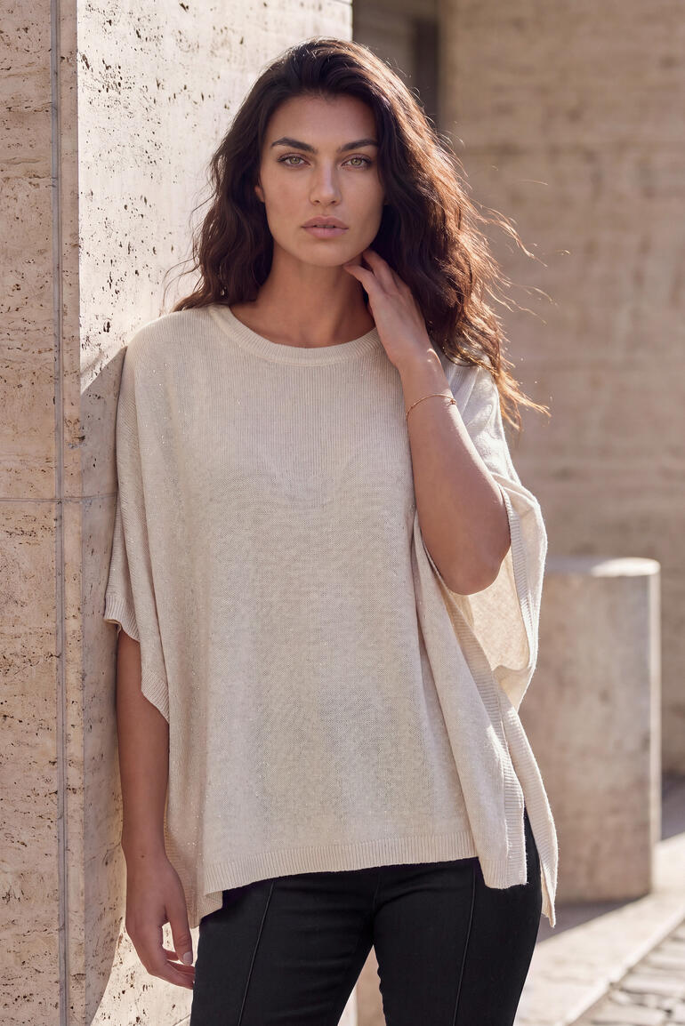 Frau in beigem Kaschmir-Glamour-Poncho vor einer Wand