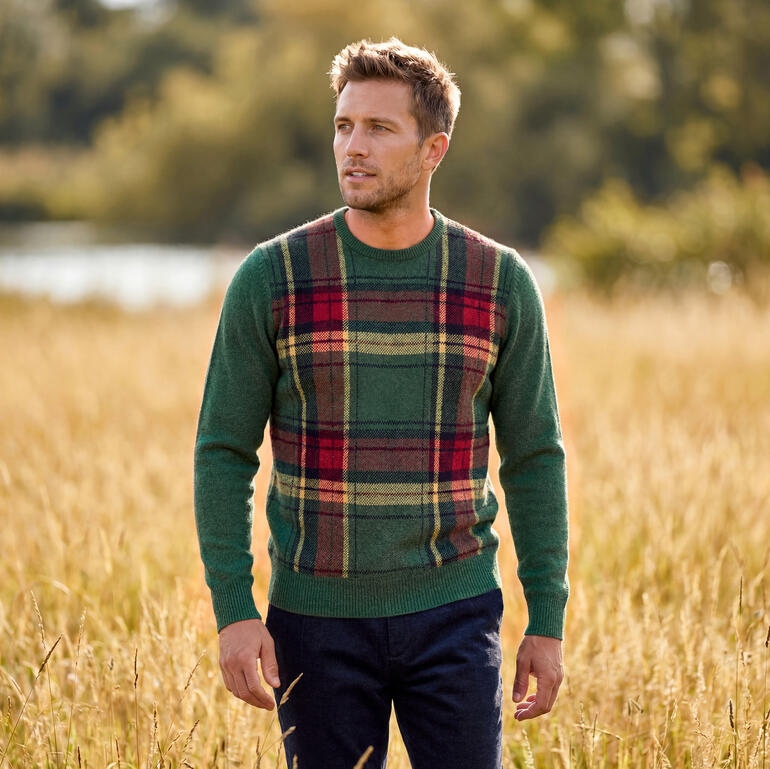 Mann in Tartan-Pullover steht im Feld