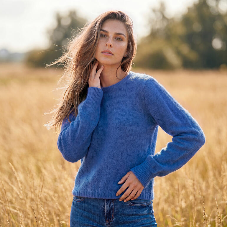 Frau in blauem Alpaka-Mohair-Pulli steht auf einem Feld.
