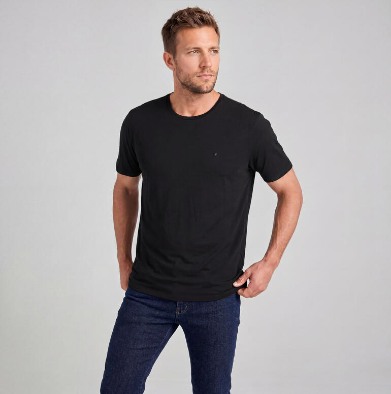 Mann in schwarzem Merino-Edel-Shirt steht vor neutralem Hintergrund.