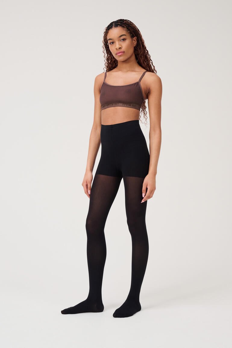 Frau trägt schwarze Beauty-Strumpfhose mit brauem Oberteil.