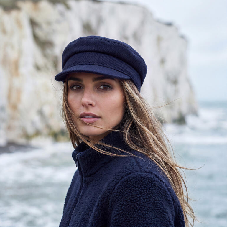 Tweed Skipper Cap in navy, getragen von einer Person am Meer.