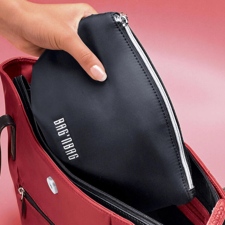 Hand, die einen schwarzen Beutel in eine rote Tasche steckt.