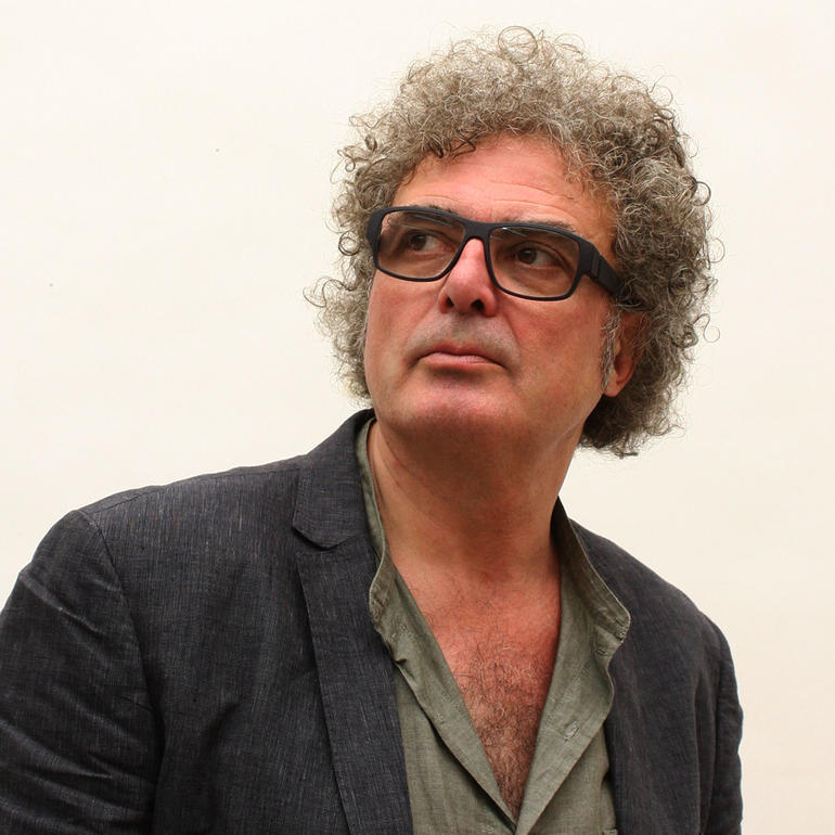 Mann mit lockigem Haar und Brille in einem grauen Blazer schaut nachdenklich zur Seite.