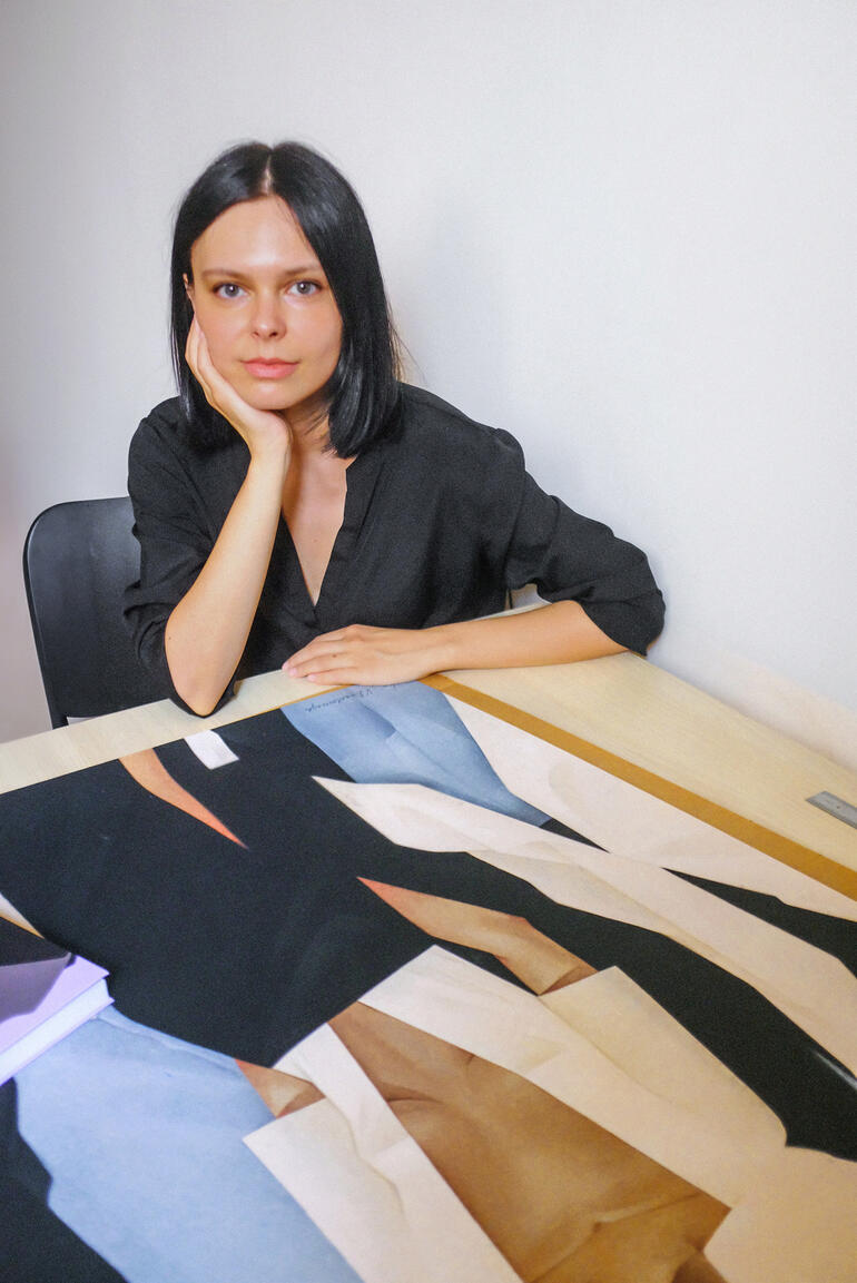 Frau mit langen Haaren sitzt an Tisch, arbeitet an Kunstwerk.