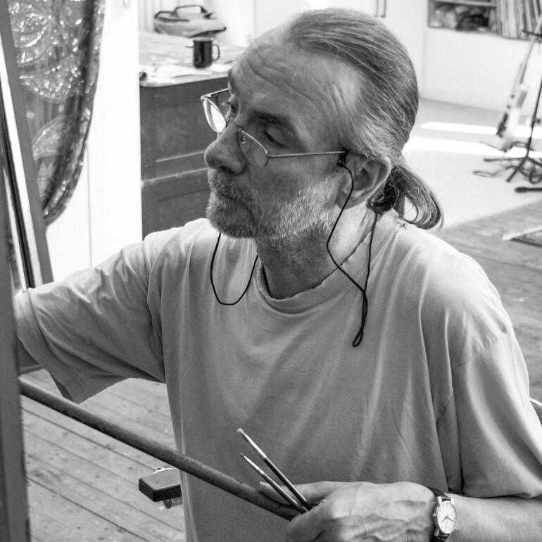 Willi Kissmer Mann malt mit Pinsel, trägt Brille und Kopfhörer.