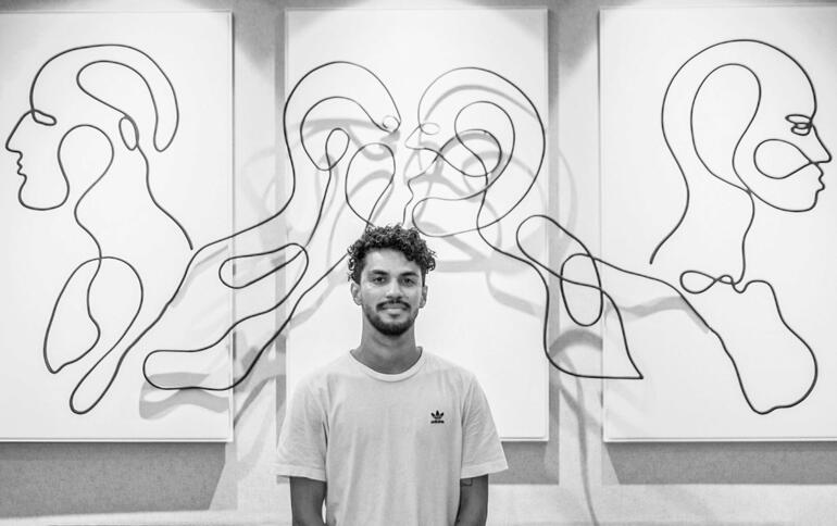 Andrés Ribón Troconis Mann steht vor Wand mit abstraktem Kunstwerk.