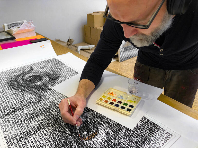 SAXA Ein Künstler malt mit Pinsel an einem großen Kunstwerk aus Text.
