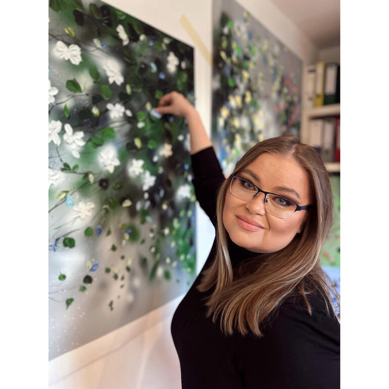 Anastassia Skopp Anastassia Skopp malt an einer Wand mit weißen Blüten.